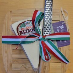 A cutting board, cheese grater and asiago cheese wedge wrapped in a red, white and green ribbon.